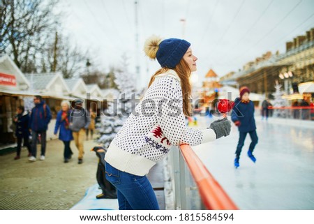 Happy young woman on Christmas market in Paris, France. Girl with red caramelized apple near skating rink. Outdoor activities on Xmas and New Year