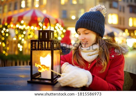 Cute young girl having rooster-shaped lollipop on traditional Christmas fair in Riga, Latvia. Child enjoying sweets, candies and gingerbread on Xmas market. Winter time with family and kids.