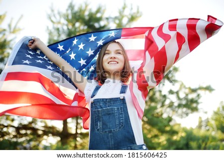 Cute young girl holding American flag outdoors on beautiful summer day. Independence Day concept. Child celebrating national holiday. Remembrance day.