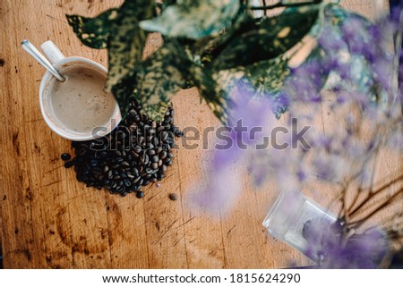 A vintage flat lay of a cup of coffee with grains of coffee near it and a plant decorating over a wood table