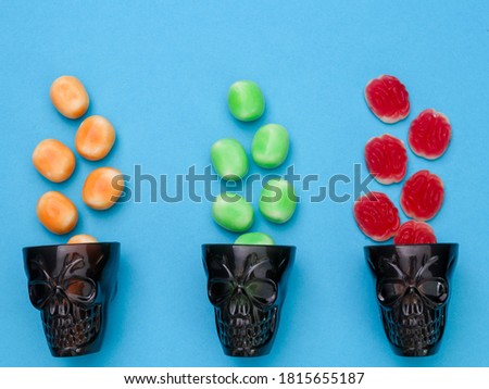 
Red, yellow and green candies for Halloween in black glasses in the shape of a skull on a blue background, top view close-up.