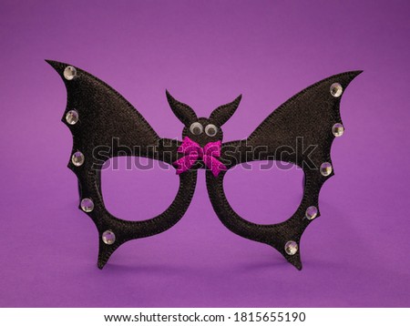 A Halloween bat with a lilac bow and rhinestones on the wings stands in the middle on a purple background, close-up side view.