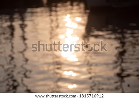 Reflections of sun and masts of a sailing vessel on the water, out of focus or blurred sea background