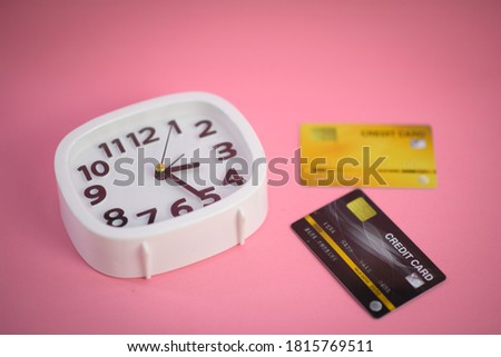 White clock with a credit card on a pink pastel background. Top view