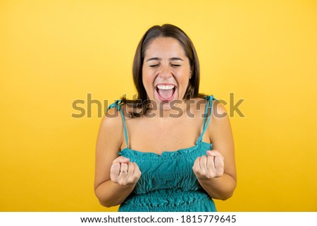 Young beautiful woman over isolated yellow background very happy and excited making winner gesture with raised arms, smiling and screaming for success.