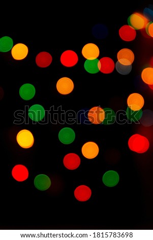 Multicolored bokeh from garlands on a black background. A versatile festive and magical backdrop. Christmas, new year, halloween. Red, yellow, green, blue circles glow in dark. Vertical, out of focus