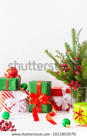 Red and green gift boxes and balls , fir tree branches and hawthorn twigs in a vase on white wall background, new year and christmas concept