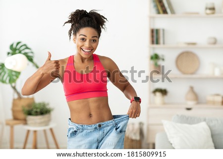 Cheerful African American Woman Showing Result Of Weight Loss Gesturing Thumbs Up Approving Diet, Wearing Old Oversize Jeans After Slimming Standing At Home, Smiling To Camera. Empty Space For Text Royalty-Free Stock Photo #1815809915