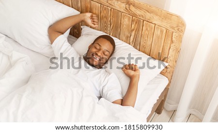 Wellslept African American Man Waking Up Stretching Hands Lying In Bed Smiling With Eyes Closed At Home. Awakening After Good Sleep In The Morning, Rest And Recreation Concept. High-Angle, Panorama Royalty-Free Stock Photo #1815809930