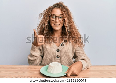 Beautiful caucasian teenager girl eating fresh white cheese smiling happy and positive, thumb up doing excellent and approval sign 