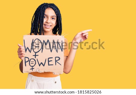 Cute african american girl holding woman power banner smiling happy pointing with hand and finger to the side 
