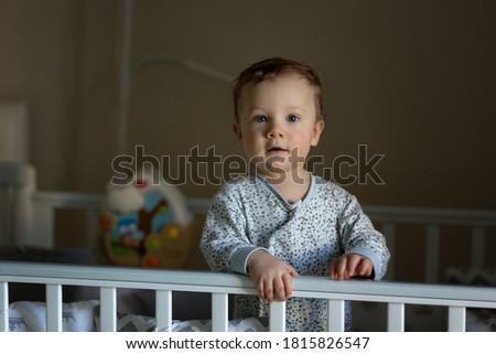 Cute baby boy in pajamas standing in a crib. Image with selective focus