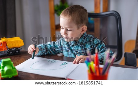Cute child boy draws with chalk on paper in an album at the table. Concept of preschool education and development of creativity