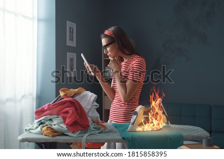 Distracted careless housewife chatting with her phone, she is burning clothes with the iron Royalty-Free Stock Photo #1815858395