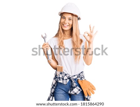 Beautiful caucasian woman with blonde hair wearing hardhat and builder clothes doing ok sign with fingers, smiling friendly gesturing excellent symbol 