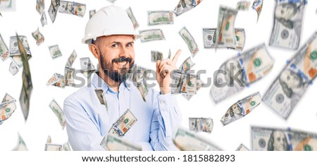 Young handsome man wearing architect hardhat with a big smile on face, pointing with hand and finger to the side looking at the camera.