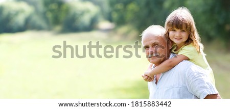 Little child girl hugs grandpa On Walk in the summer outdoors. Concept of friendly family. copy space. banner
