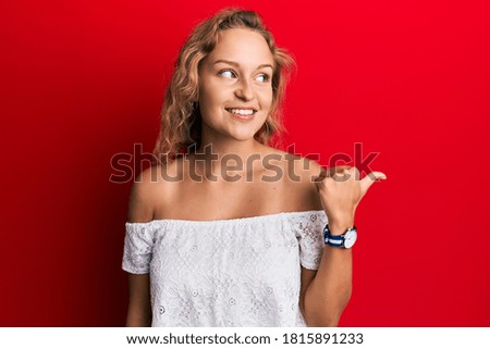 Beautiful caucasian woman wearing casual clothes over red background smiling with happy face looking and pointing to the side with thumb up. 