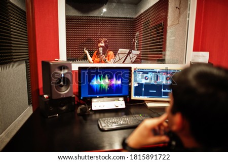 Young asian singer with microphone recording song in record music studio with sound producer.