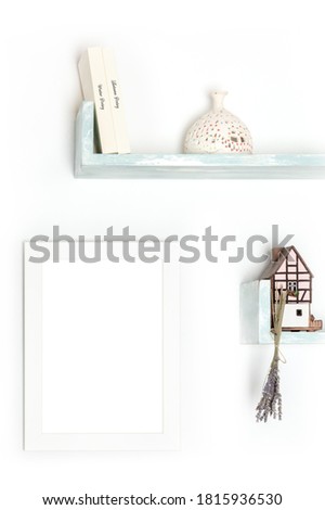 Poster mock-up. A blank frame on a wall with books and objects on a white wall