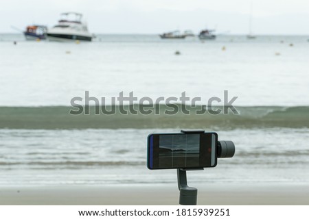 Closeup smarthphone on gimbal filming the beach and boats.