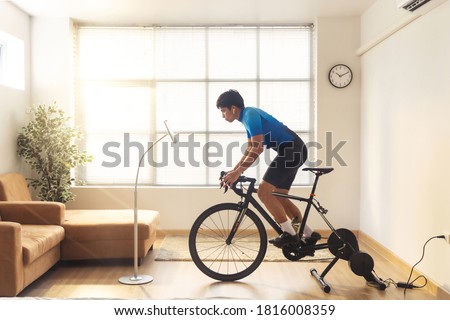 Asian man cyclist. he is exercising in the house and  trainer and play online bike games.He stood up spinning Royalty-Free Stock Photo #1816008359