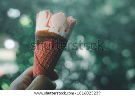 Ice cream strawberry wafer in hand against on nature blur background. Close up