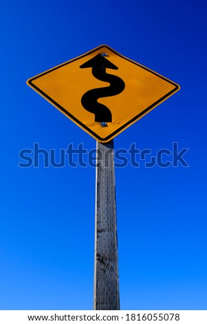 Curves ahead on roadsign road sign bright yellow on blue sky