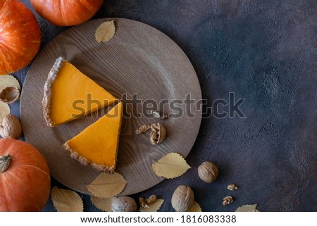 Two pieces of pumpkin pie on a wooden plate surrounded by pumpkins, walnuts and autumn leaves