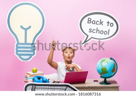 Excited kid having idea while sitting near gadgets, books and paper artwork on pink background