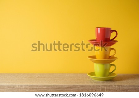 Coffee cups on wooden shelf over yellow wall background