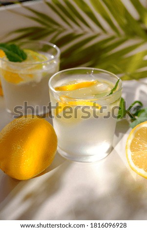 Lemon water with fresh lemons and green plants