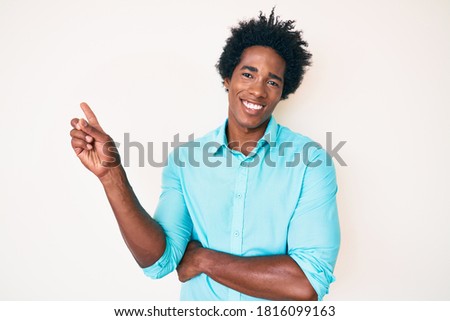 Handsome african american man with afro hair wearing casual clothes with a big smile on face, pointing with hand and finger to the side looking at the camera. 