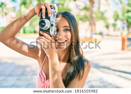 Young hispanic woman smiling happy using vintage camera standing at the park.