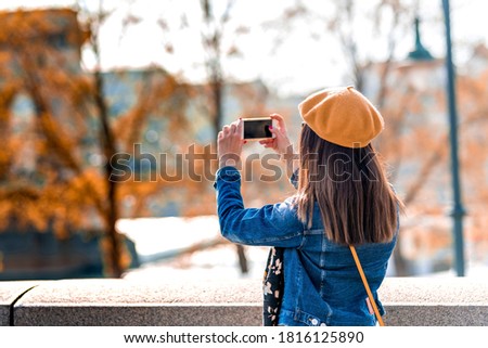 A beautiful woman taking pictures in a city park during spring or autumn.