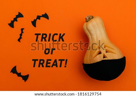 Halloween pumpkin in black protective medical mask and bats from black paper on orange background.Inscription TRICK AND TREAT! on an orange background.Halloween and covid-19 concept.