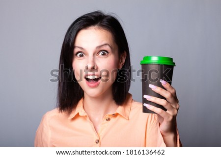 cute girl in an orange shirt holds a cup of coffee in her hands, gray background