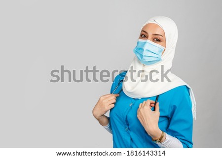 Portrait of a friendly Muslim doctor or nurse in hijab, mask on a gray background.