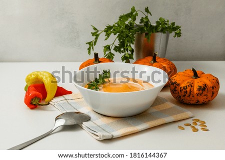 A bowl of pumpkin or carrot vegetarian cream soup is garnished with fresh parsley and cream on a white textured table. selective focus