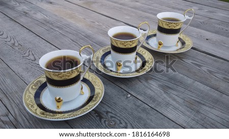 Three thin China coffee cups and gold-edged saucers on a gray, rough wooden table