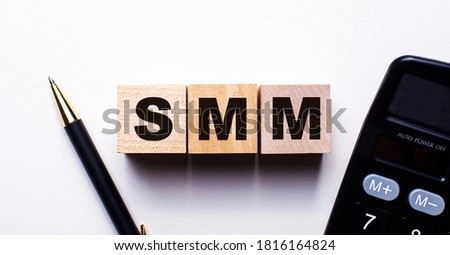 SMM is written on wooden cubes on a light background between a calculator and a pen. IT content