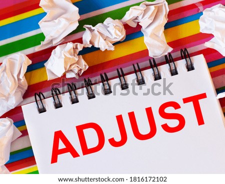 The word ADJUST is written on a white card with a bright striped background. Nearby white crumpled pieces of paper