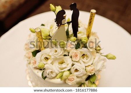 beautiful white wedding cake decorated with flowers and roses with black figures of the bride and groom. Wedding decor