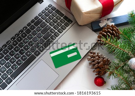 Christmas shopping online with a green credit card and laptop for the Christmas holidays. Black Friday. Christmas decorations, gifts, notebook, white marble background.