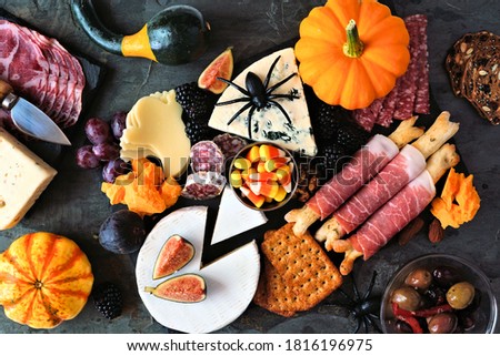 Halloween theme charcuterie platter. Top view table scene against a black stone background. Assorted cheese and meat appetizers.