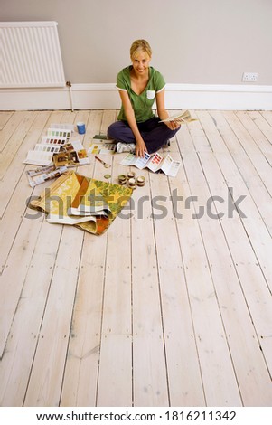 Woman holding a color swatch sitting on floor and looking at the camera.