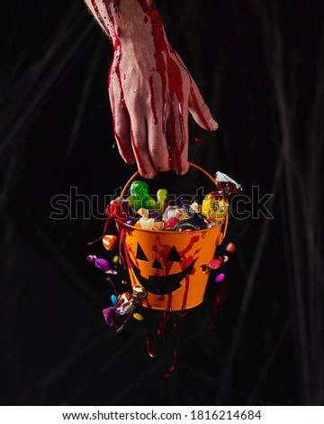 A bloody hand holds  a bucket of sweets candy. Halloween background