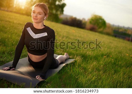Girl practices yoga fitness exercise outdoor on the grass and yoga mat in earphones. Woman doing Urdhva mukha shvanasana exercise, upward facing dog pose, working out.