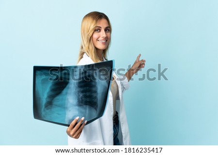 Young blonde Uruguayan doctor woman isolated on blue background pointing back