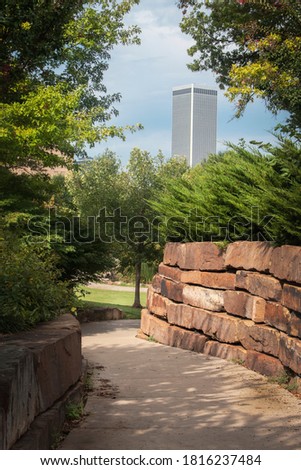 Tall skyscraper in distance of curving rock walled sidewalk through wooded urban park